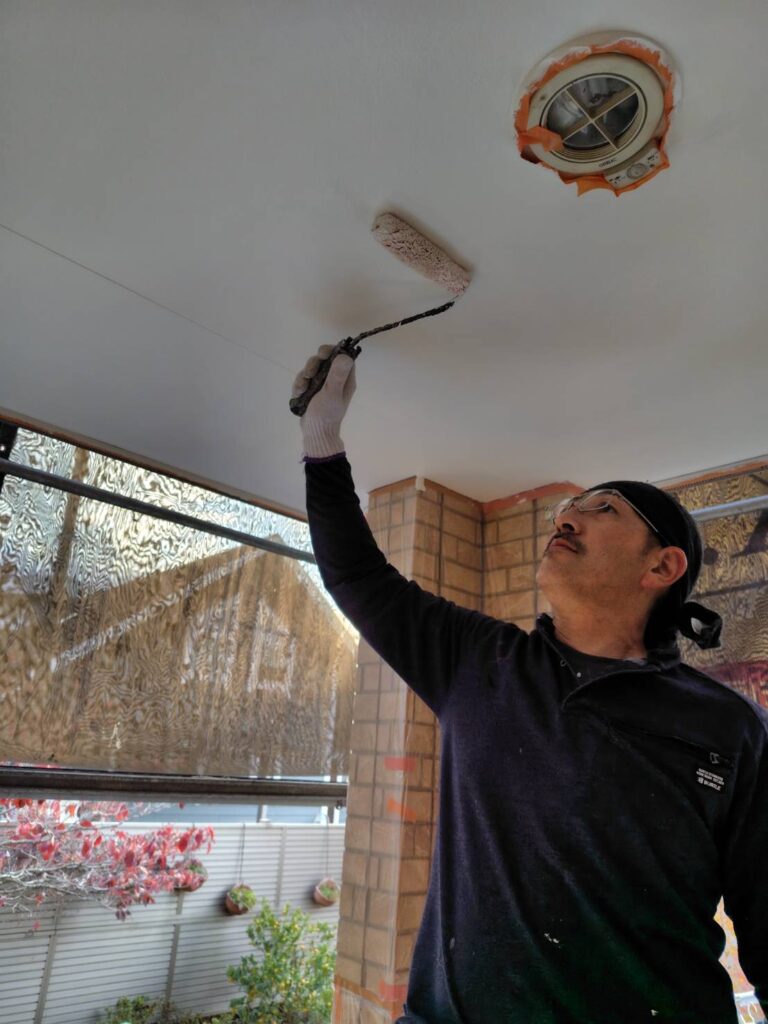 職人による軒天の塗装作業の様子。刷毛やローラーを使い、丁寧に塗料を塗布している。