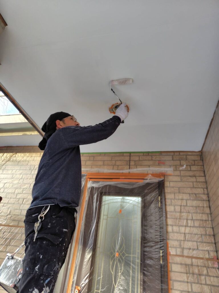 職人による軒天の塗装作業の様子。刷毛やローラーを使い、丁寧に塗料を塗布している。