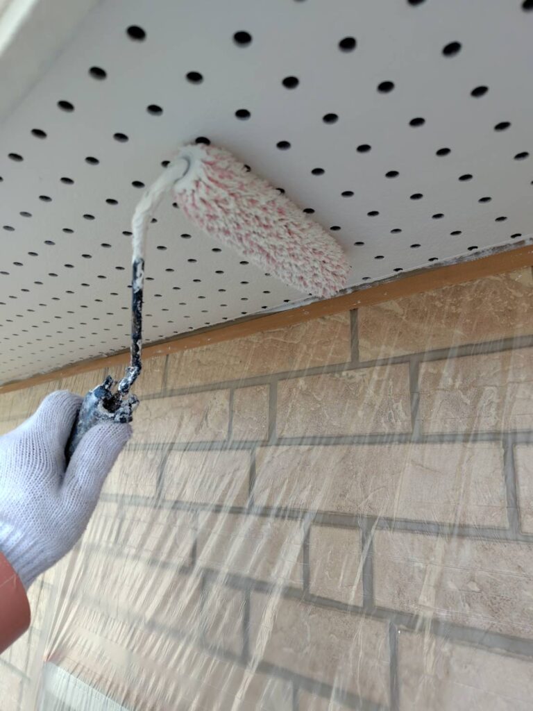 職人による軒天の塗装作業の様子。刷毛やローラーを使い、丁寧に塗料を塗布している。