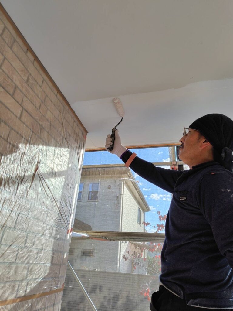 職人による軒天の塗装作業の様子。刷毛やローラーを使い、丁寧に塗料を塗布している。