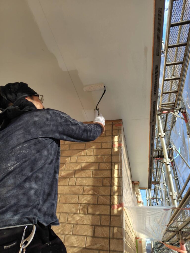 職人による軒天の塗装作業の様子。刷毛やローラーを使い、丁寧に塗料を塗布している。