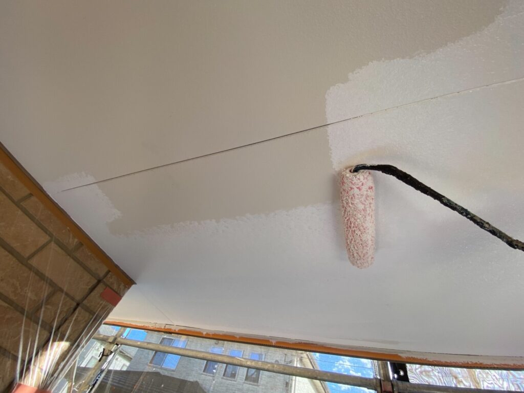 職人による軒天の塗装作業の様子。刷毛やローラーを使い、丁寧に塗料を塗布している。