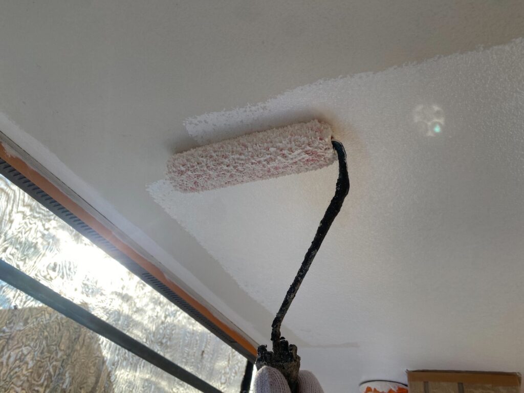 職人による軒天の塗装作業の様子。刷毛やローラーを使い、丁寧に塗料を塗布している。