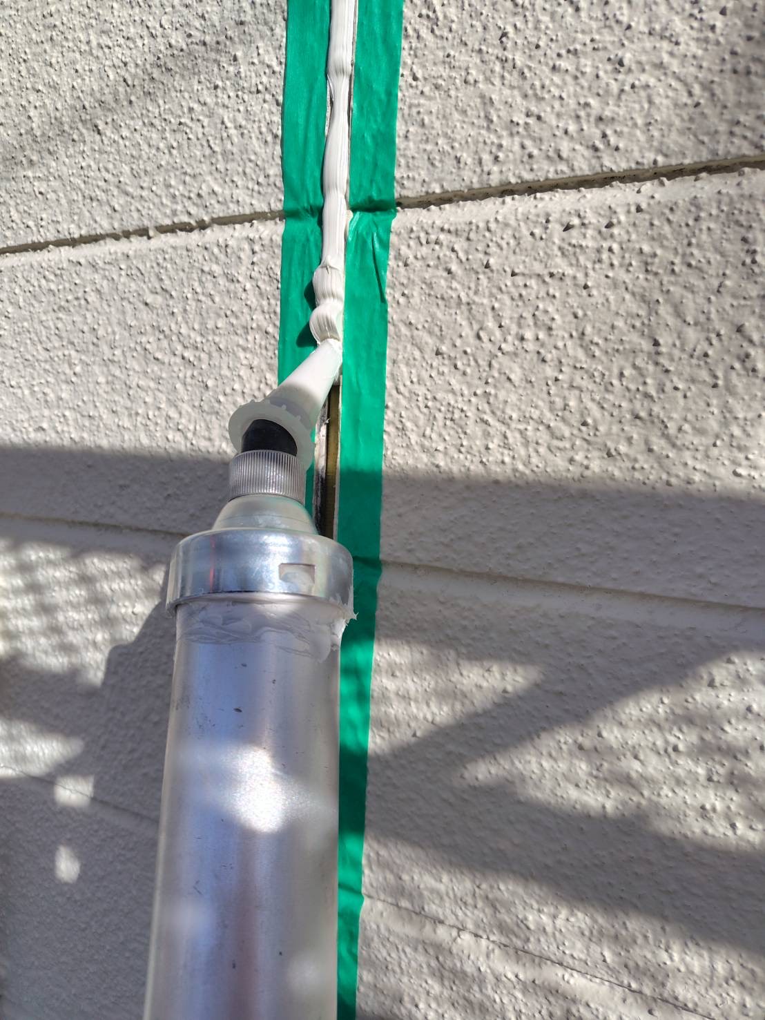 外壁の目地に専用のコーキングガンを使って、新しいコーキング材を注入している様子。