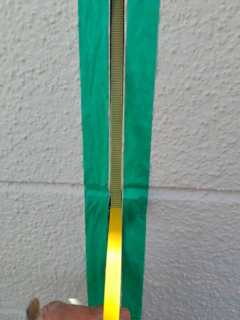 養生された目地の底に、3面接着を防止するための黄色い絶縁テープ(ボンドブレーカー)を貼る作業。