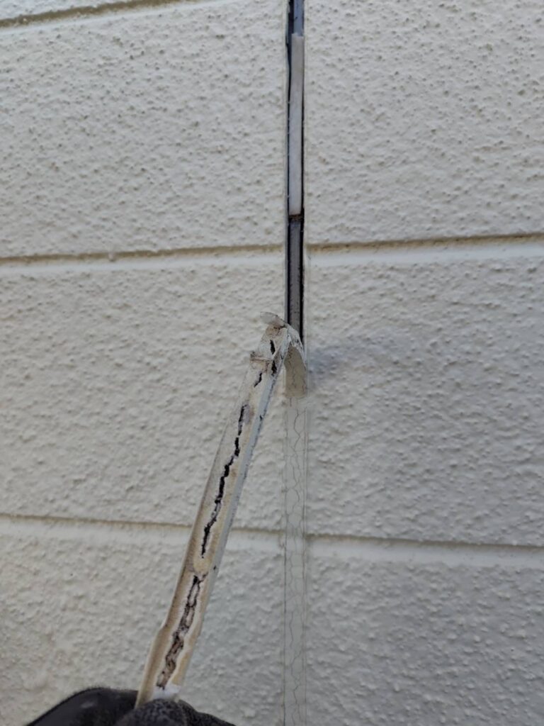 カッター等を使用して、ひび割れた古いコーキング材を外壁から剝がし取り除いてる様子。