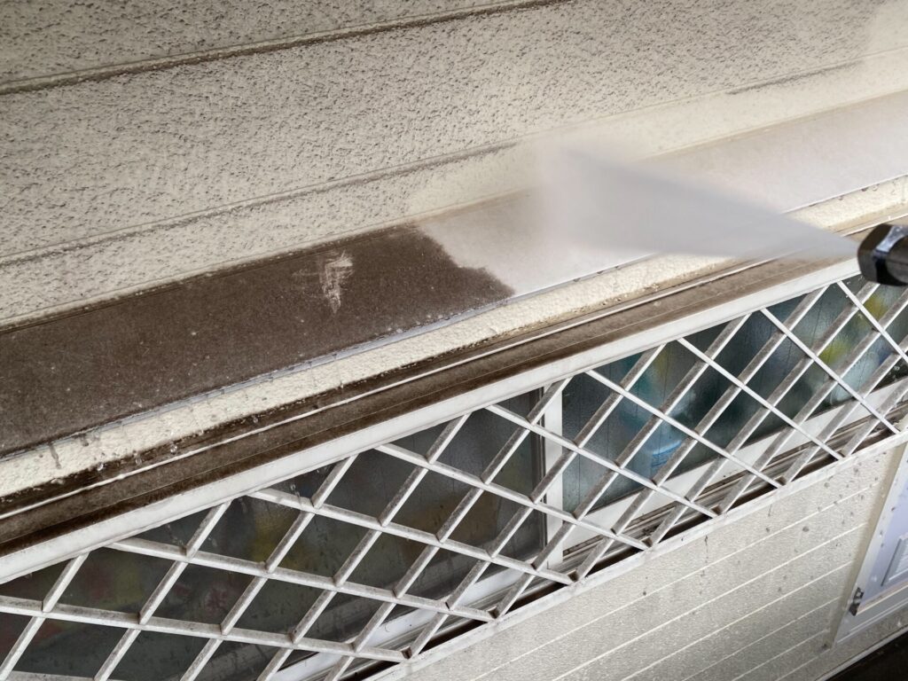  窓まわりの高圧洗浄：サッシ上の水切り板に溜まった長年の泥汚れを強力な水圧で除去する様子