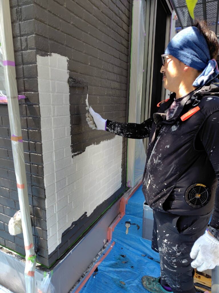 外壁デザイン部分に濃色の塗料をローラーで中塗り塗装する作業風景