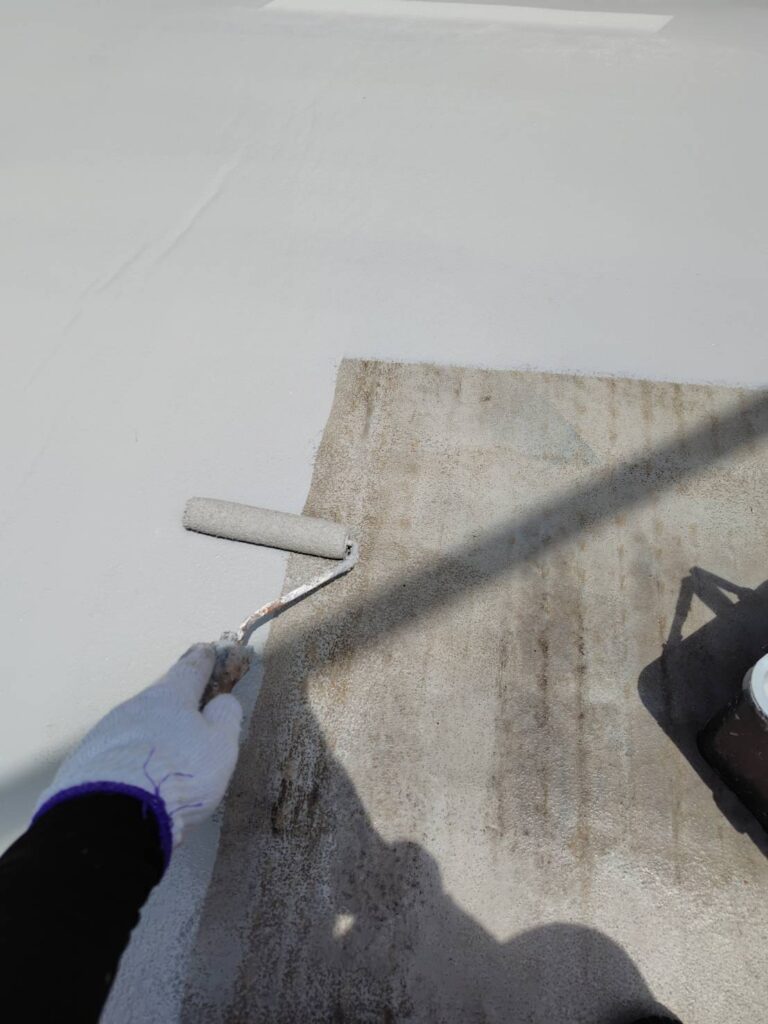 ローラーを使用しベランダ防水床へトップコートを塗り広げている施工風景