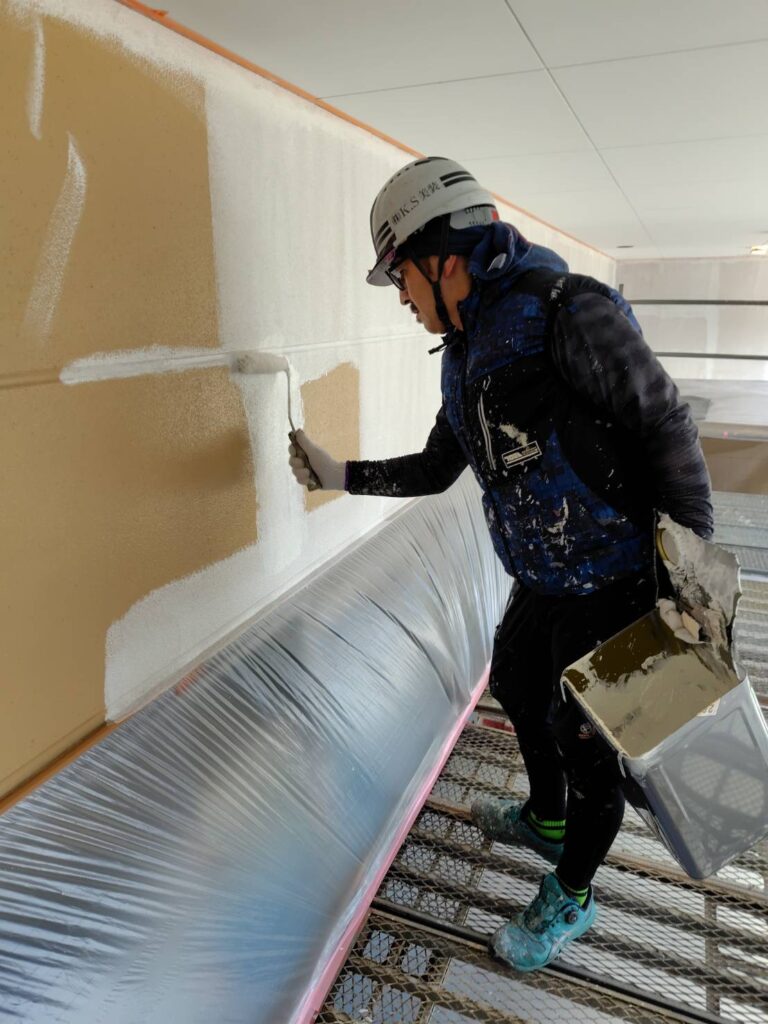ヘルメットを着用した職人が世田谷区の商業施設外壁へ下塗りを行う様子