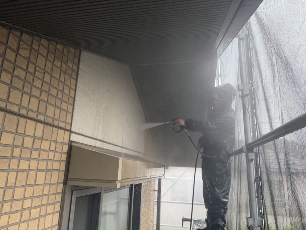 足場上でレインウェアを着用し外壁上部と軒天の汚れを高圧洗浄する職人